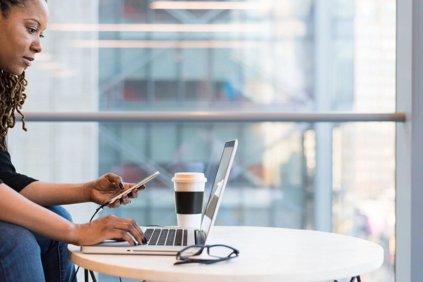 Mulher trabalhando em um notebook e consultando o celular em um escritório.